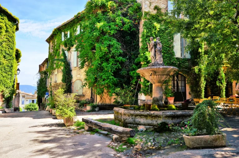 Begrünter Stadtplatz mit Brunnen in einem malerischen Dorf in der Provence, Frankreich